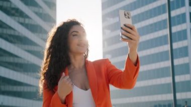 Mutlu Afrikalı Amerikalı kadın nüfuzlu blogcu cep telefonu kullanıyor, selfie çekiyor, sosyal medya uygulamalarına yüklüyor, arkadaşlarıyla internet üzerinden sohbet ediyor altın güneş ışığı altında şehir merkezinde duruyor.