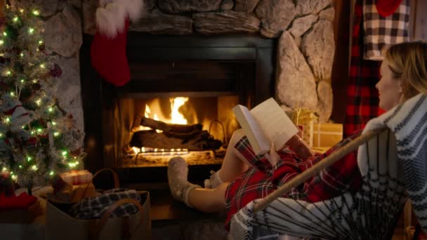크리스마스를 꾸며진 집에서 아늑한 불타는 벽난로에서 휴식을 취하는 여자의 의자에 — 비디오