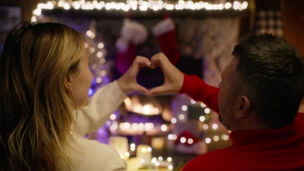 ハッピーカップルが心臓を形作る関節指を通して暖炉を見ている様子 ロマンチックなクリスマスイブのお祝い 結婚した配偶者を愛する 誠実な感情と愛のコンセプト4K — ストック動画