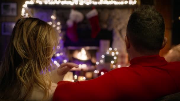 女朋友和男朋友紧紧地拥抱在一起 温柔地望着对方 一对浪漫的夫妇在圣诞前夜坐在客厅的沙发上 看着篝火熊熊燃烧 — 图库视频影像
