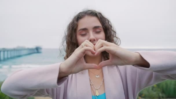 接近肖像画20岁的欧洲女人展示出心脏的迹象 用手做记号 可爱的女孩感激地笑着看着站在室外的相机 善举志愿者 — 图库视频影像