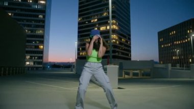 Canlı kamera hareketleri ile çılgın funky ruh hali, çok ırklı dansçı eğlenceli sokak dansı yapıyor yavaş çekim. Uzun kıvırcık saçlı, çatıda dans eden komik kadın şehir merkezinde eğleniyor.
