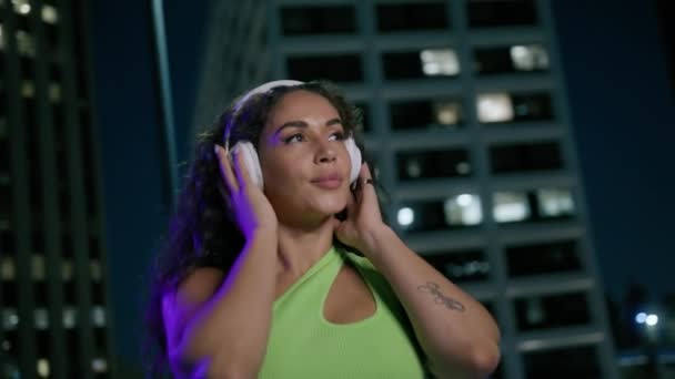 快乐性感的非洲裔美国女人戴着耳机独自在夜市街道上跳舞 在市中心听音乐的年轻女子嬉皮士轻松自在地享受着户外的夜城4K — 图库视频影像