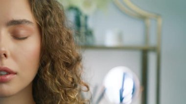 People close up slow motion. Half Face portrait of young beautiful curly model with closed eyes. Pretty girl opening eyes and looking straight to camera in modern apartment on blurred copy background