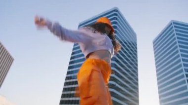 Hip-hop kraliçesi twerk yapıyor. Breakdansçı kadın günbatımının tadını çıkarıyor. Spor kıyafetli neşeli çok ırklı kız şık turuncu kargo pantolonları ve şehir merkezinde dans ederek müziğe dönüşen kova şapka giyiyor.