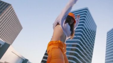 Hip-hop kraliçesi twerk yapıyor. Breakdansçı kadın günbatımının tadını çıkarıyor. Spor kıyafetli neşeli çok ırklı kız şık turuncu kargo pantolonları ve şehir merkezinde dans ederek müziğe dönüşen kova şapka giyiyor.