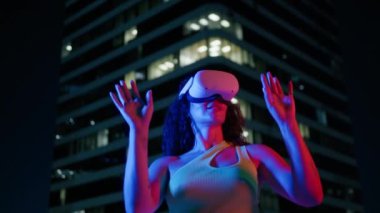 Gelecekteki VR eğitim teknolojisi konsepti. Genç siyahi kadın gece şehir arka planında sanal gerçeklik kulaklığı kullanıyor. Eğlence teknolojileri. Gelecekteki çeşitlilik insanlar yavaş çekim 4K RED