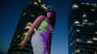 Arka plandaki gökdelenlerde kamera önünde dans eden seksi kadın. Neşeli kadın çatıda müzik eşliğinde el sıkışıyor. Yakından güzel bir kız. Gün batımı diskosunda eğleniyor.