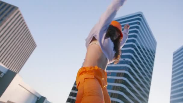 ヒップホップ クイーンがタイガーを作る 日没4Kを楽しんでいるブレイクダンサーの女性 トレンディな明るいオレンジ色の貨物パンツとバケツの帽子を身に着けているスポーツ服の楽しい多種多様な少女は ダウンタウンで音楽に踊ります — ストック動画