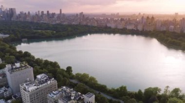 New York şehir merkezi arka planı. Şehir parkı yaz seyahati. Central Park 'ın üzerinde destansı pembe gün batımı. Manzaralı göl güzel gökyüzünü yansıtıyor. Yeşil Kentsel Central Park Antenleri. Manhattan 'ın 4K epik manzarası