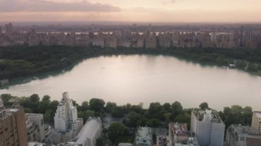 Yeşil park ve binalarla çevrili güzel bir göl. Sinematik Central Park manzara manzarası. New York şehir merkezinin 4K hava görüntüsü. Manhattan gökdelenleri arka planda yeşil şehir parkı
