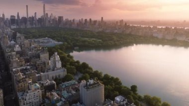 Yeşil Kentsel Central Park Antenleri. Manhattan 'ın 4K destansı manzarası. New York şehir merkezi arka planı. Şehir parkı yaz seyahati. Central Park 'ın üzerinde destansı pembe gün batımı. Manzaralı göl güzel gökyüzünü yansıtıyor