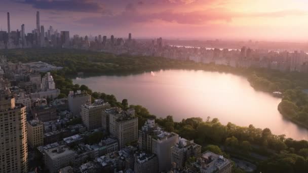 中央公园上方的史诗般的粉色落日 风景秀丽的湖面映衬着美丽的天空 绿城中央公园的空中 4K史诗全景曼哈顿 纽约市中心的背景 市区公园暑期旅游 — 图库视频影像