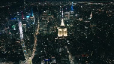 New York şehrinin arka planında büyülü bir yaz gecesinde sokaklarda uçmak. Gece vakti Manhattan 'daki Empire State Binası' nın gökdelenlerle çevrili havadan çekilmiş görüntüsü.