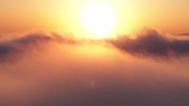 Altın gün doğumunda, bulutların üzerinde, yoğun sisten yükselen bir kamera. Güneş ufuktan ufka kadar sonsuz bulut denizinin üzerinde yükseliyor. İnanılmaz doğa deniz manzarası 4K İHA gökyüzünde.