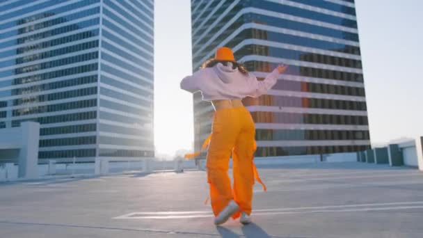 身穿运动服 身穿时髦鲜艳橙色货物裤子 头戴斗篷帽的多种族女孩在市中心欢快地跳着舞曲 Hip Hop皇后做Twerk 日落时分吃早餐的女人4K — 图库视频影像
