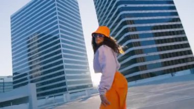 Seksi Twerk ve serbest stil dansçısı şehrin arka planında altın günbatımında dans figürleri yapıyor. Afrikalı Amerikalı genç bir kadın çatıda şehvetle dans ediyor.