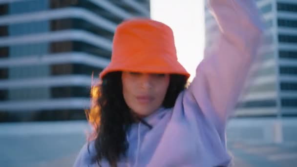 迷人而又酷的黑发多民族女人 戴着鲜亮的橙色帽子 四处跳舞 手舞足蹈 在城市背景下欣赏日落4K红色相机 — 图库视频影像