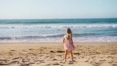 Küçük kız kumsalda eğleniyor. Sıcak ve güneşli bir yaz gününde okyanus kıyısında oynayan kız çocuğu. Yaz tatili konsepti yavaş çekimde ve arka planda. Mutlu aile, aşk, rüya gören çocuk konsepti 4K