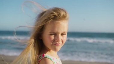 Küçük kızın portresini yakından çek. Ciddi ciddi kameraya bak. Yaz günbatımında okyanus sahilinde dur. Düşünceli meraklı çocuk dışarıdaki kameraya bakıyor. Tatlı yüz mavi gözler, güçlü yüz ifadesi.