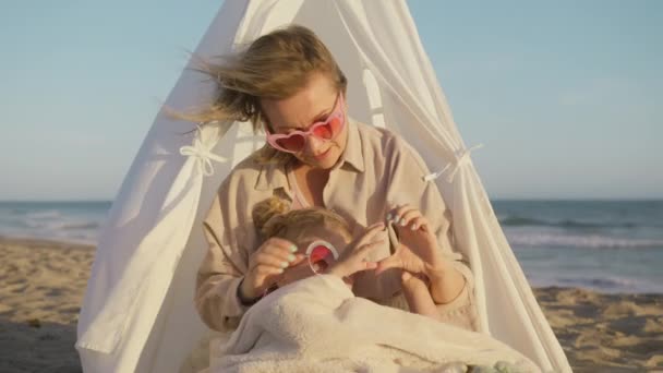 充满爱心的年轻女性妈妈和可爱可爱可爱的小女孩在金色的夕阳下坐在海滩上做心形手势 爱的家庭结合欢笑 爱的概念结合在一起 — 图库视频影像