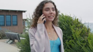 Gülümseyen güzel bir kadın okyanusta cep telefonunu arıyor. Dost canlısı kıvırcık bayanın portresi akıllı telefon 4K ile yürüyor. Kapalı alan pozitif kadın günlük giysiler içinde yaz parkında akıllı telefonlardan konuşuyor.