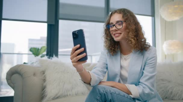 モダンオフィスで働くビデオチャットのためのフロントモバイルカメラを使用して携帯電話で話している若いビジネス女性 アパート4Kに座っている携帯電話で電話をするスーツを着ているビジネスマネージャー — ストック動画