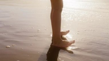 Çıplak ayaklı çocuğun okyanus dalgalarında koşup suya atlamasını yakından izle. Gün batımında eğlenen tatlı küçük kız. Çiçekli uzun sarı saçlı sevimli bebek. Okyanus sahilinde doğanın tadını çıkarıyor.