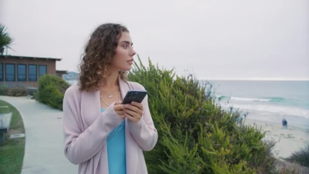 夏天公园里穿着休闲装 头戴智能手机的衣冠楚楚的女人在户外聊天 微笑的女商人在海上打电话给手机 带着智能手机4K走的友善卷曲女士的画像 — 图库视频影像