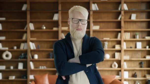 自信を持ったアルビノの実業家がオフィスで手を横切る 図書館にいるスマートな起業家 眼鏡を閉じている真面目な男性の肖像画 カメラにポーズするブロンド男 スローモーション — ストック動画