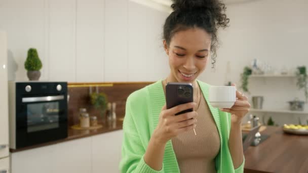 Wielorasowe Kręcone Kobieta Picie Kawy Trzymając Smartfona Wybrać Towary Internecie — Wideo stockowe