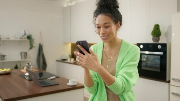 笑着多种族女人看前面的相机手机 享受现代科技站在现代厨房 现代真人生活方式使用智能手机在线聊天视频通话4K — 图库视频影像
