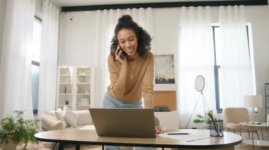 Pozitif küçük işletme sahibi yönetim projesi ve çoklu görev 4K. Genç yetişkin Afro-Amerikan bayan girişimci laptopta çalışıyor ve dahili ofisteki müşteri ya da ortakla konuşuyor