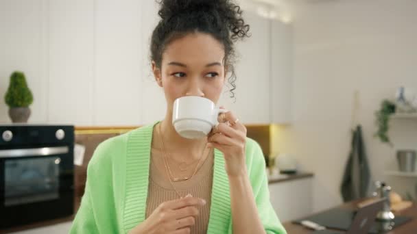渴望微笑的20多岁多种族女人开始新的一天 一杯芬芳的咖啡 独自站在现代厨房的内部 近距离饮用白杯的不同模式 人们的生活方式为4K — 图库视频影像