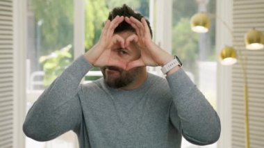 Yakışıklı, komik, beyaz bir adamın portresi sevgi dolu bir el hareketi gösteriyor. Mutlu komedyen genç adam aşk işareti gösteriyor, aptal yüz ifadesiyle şaka yapıyor. Kırmızı Kamera 4K 'da romantik eğlence ve mizah konsepti.