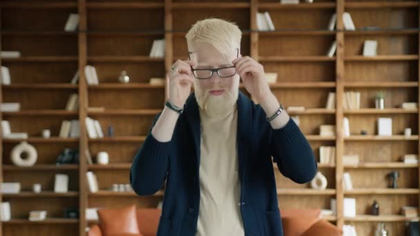 図書館で眼鏡をかけているアルビノの男性の肖像画 オフィスで手を横断する疲れたビジネスマン 思慮深い表情のスマートな男 若い起業家は 起きてから疲れを感じる — ストック動画