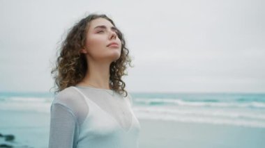 Yan görünüm kızı huzur, zihinsel rahatlama, stres yok. Sakin genç bir kadın derin bir nefes alıyor. Gözleri kapalı meditasyon yapıyor. Arka plandaki okyanus dalgalarına bakıyor.