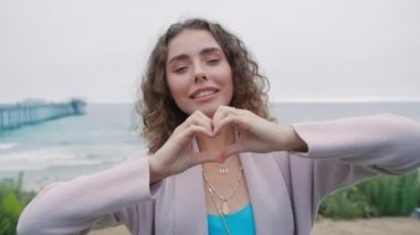 Sevgi, teşekkür ederim, minnet, destek, iyilik gönüllüsü konsepti. 20 'lerin Avrupalı kadın portresini kapat. Kalp işaretini göster. Ellerle sembol yap. Şirin kız okyanusa gülümseyen kameraya baktığı için minnettar.
