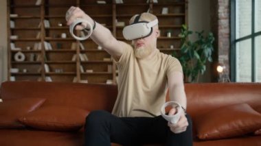 Genç yakışıklı adam etrafına bakıyor ve joysticklerle sanal silah ateşliyor. VR gözlüklü sanal oyuncular modern çatı katı tarzı dairelerde sanal gerçeklik oyunu oynarlar. Hippi sakallı adam oyun konsepti
