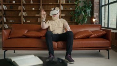 Modern çatı katında çalışan heyecanlı beyaz tenli genç adam VR gözlük takıp ellerini havaya kaldırıyor. Girişimci sanal gerçeklik kulaklığı kullanarak proje üzerinde çalışır. Teknoloji konsepti