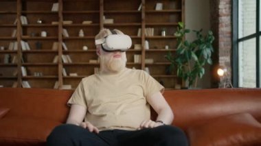 Gelişmiş gerçeklik deneyimi için sanal gerçeklik kulaklığı takan yakışıklı genç hippi. Adam bir şeye dokunuyor modern 3D VR Google 'ı kapalı alanda kullanıyor güneşli bir günde AR gözlüğü kullanıyor 4K