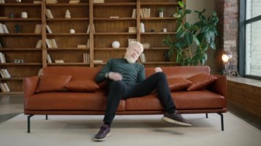 Neşeli hippi albino adam görünmez gitar çalıyor modern çatı katındaki kanepede eğleniyor. Modern eğlence, müzik ve mutlu gençler konsepti. Rüyalarının derinliklerinde kendinden geçmiş bir erkek 4K