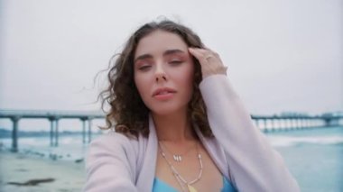 Moda blogunda paylaşmak için mobil uygulama üzerinden popüler sosyal medya içeriği yaratan güzel kıvırcık kız. Selfie POV yakından bakın. Okyanus sahilinde özçekim yapan, eşsiz açık mavi gözlü, gülümseyen genç bir kadın.