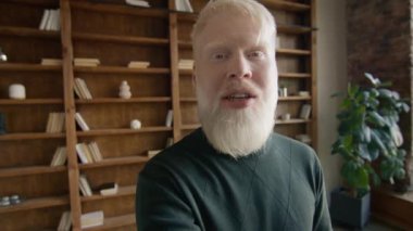 İnternette arkadaşlarıyla sohbet eden bir sürü pozitif albino adam. Gülümseyen iş adamı iş arkadaşıyla çevrimiçi konuşuyor. Arkaplanda kütüphane kitaplığı raflarıyla görüntülü konuşma yapan genç adam