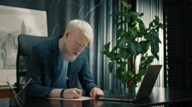Kendinden emin bir albino girişimcisi iş yerindeki kağıtlara not alıyor. İş yerinde dizüstü bilgisayar kullanan bir erkek işadamı. Belgelerle ilgili çalışmalara odaklanan ciddi bir yönetici. Ofiste çalışan bir çalışan. 