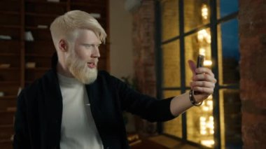 Gülümseyen albino işadamı akıllı telefondaki online konferansta el sallıyor. Müşteriyle görüntülü konuşma yapan sıradan bir CEO gece yarısı tavan arası penceresinde parlayan sokak tabelasında görülüyor. Freelancer el sallıyor.