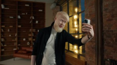Sıradan bir albino işadamı selfie çekiyor V işareti gösteriyor, hepsi de gece yarısı akıllı telefondaki güzel fotoğraflar. Gülümseyen olumlu adam. Yakışıklı hippi barış sembolü gösteriyor. Adam selfie için poz değiştiriyor.