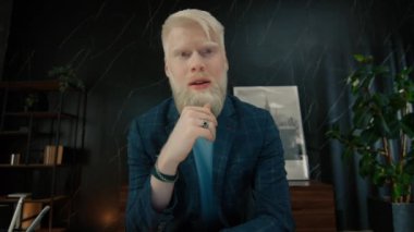 Genç albino işadamı ofiste müşteriyle çevrimiçi görüşme yapıyor. Şaşırmış yüz ifadesi olan bir erkek yönetici. Gülümseyen menajer evet diyor. CEO meslektaşlarıyla yeni bir girişimi tartışıyor