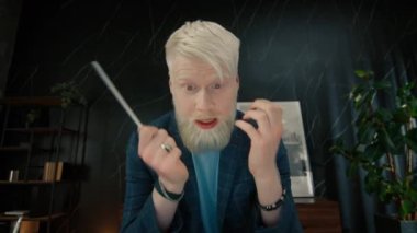 Çevrimiçi video konferansı sırasında iş arkadaşlarıyla tartışan agresif bir albino girişimcisi. Öfkeli iş adamı modern ofiste görüntülü sohbet yoluyla konuşuyor. Erkek yönetici kalemle el kol hareketi yapıyor.