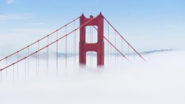 Güneşli sisli günde dünyaca ünlü manzaranın destansı manzarası. San Francisco, Kaliforniya 'daki Golden Gate Köprüsü' nün yüksek kırmızı kulelerini çevreleyen ağır beyaz sisli sinematik hava görüntüleri.